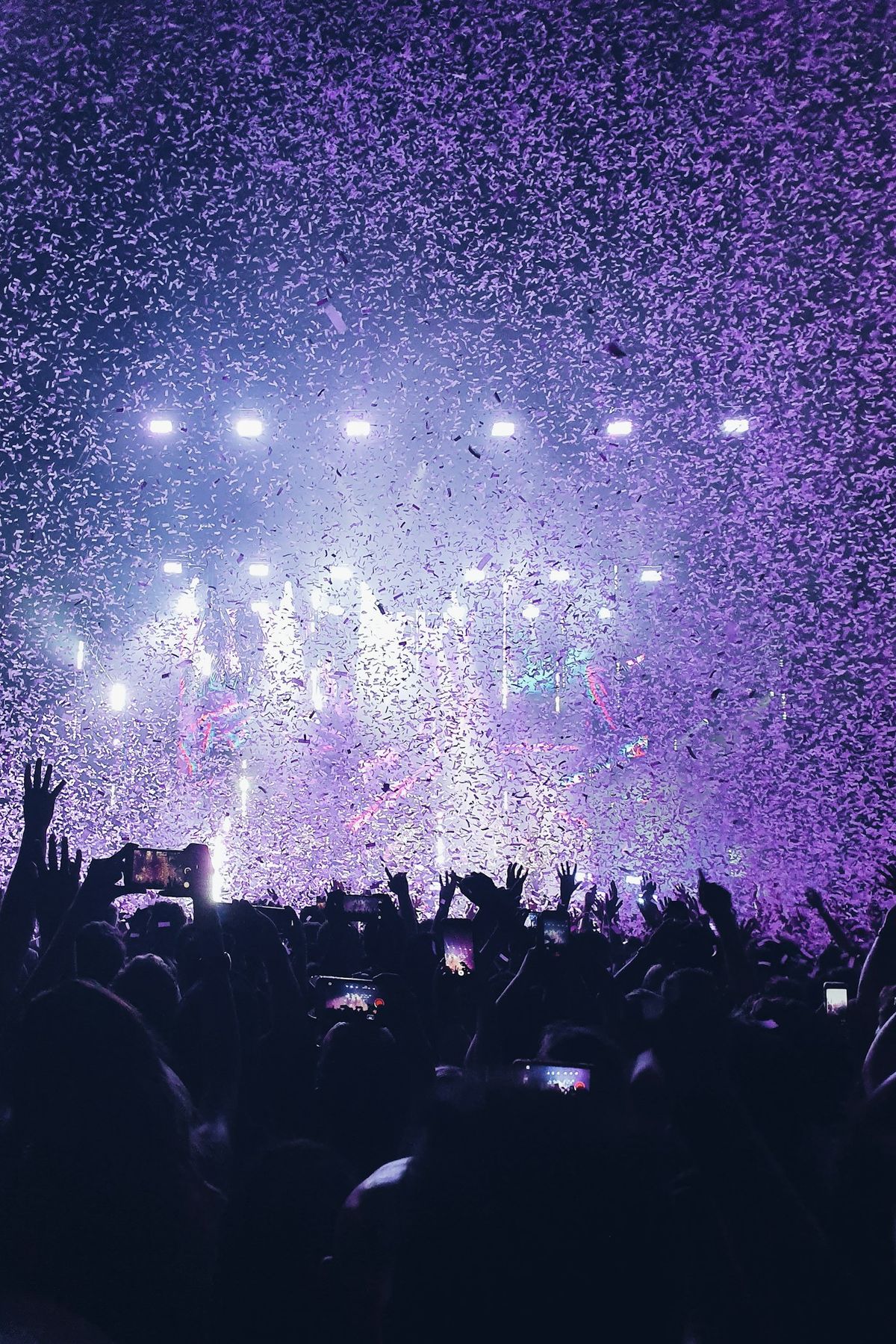 Confetti falls over a crowd facing a stage washed in light